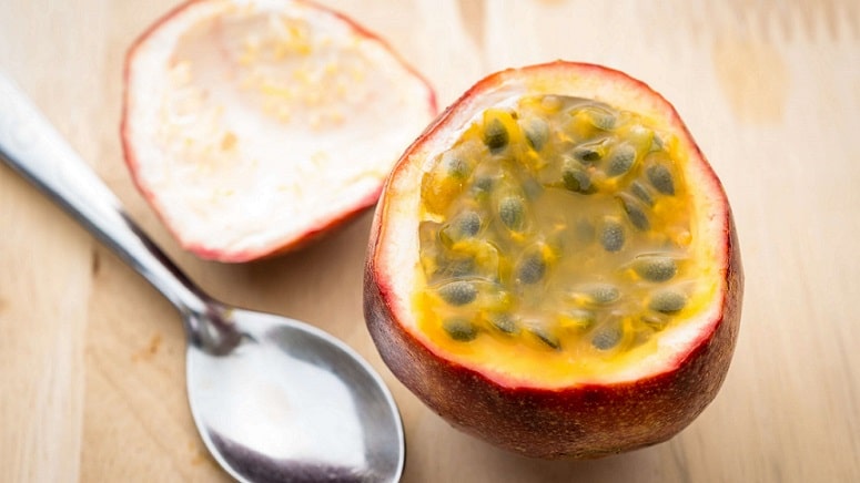 A purple passion fruit with seeds and spoon